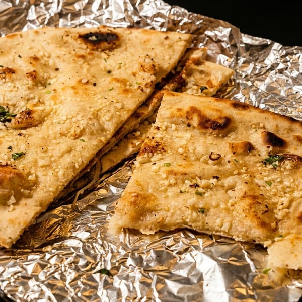 Garlic naan bread, cut into pieces, resting on crinkled aluminum foil.
