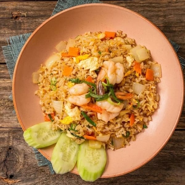 Shrimp fried rice with vegetables and egg, garnished with cucumber slices on a pink plate.