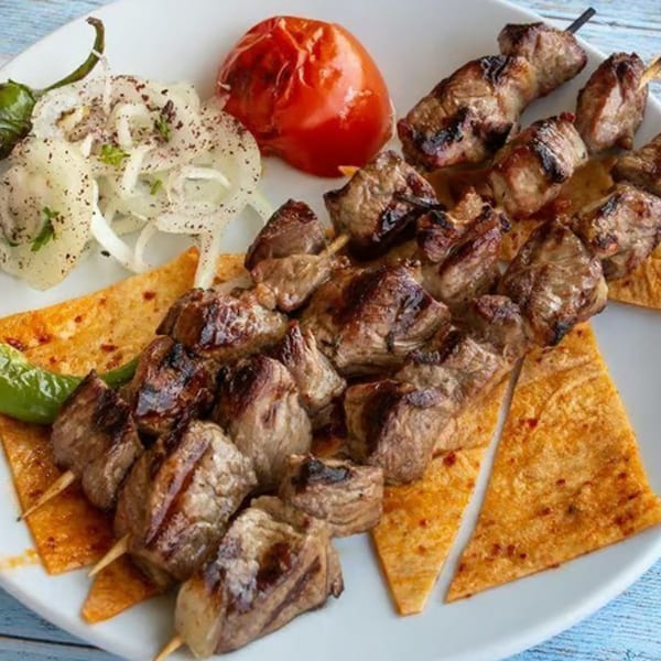Grilled meat skewers with roasted tomato, sliced onions, and flatbread on a white plate.