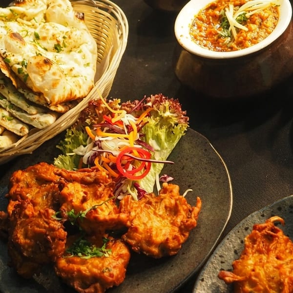 A spread of Indian dishes including naan bread, pakoras with salad, and two bowls of curry.