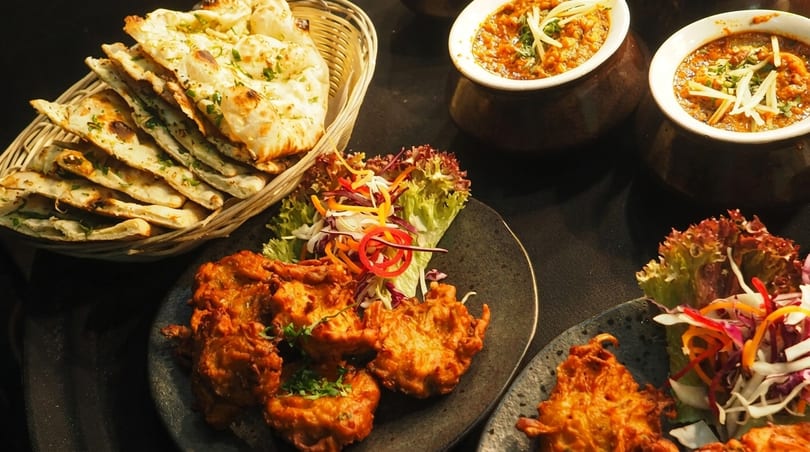A spread of Indian dishes including naan bread, pakoras with salad, and two bowls of curry.